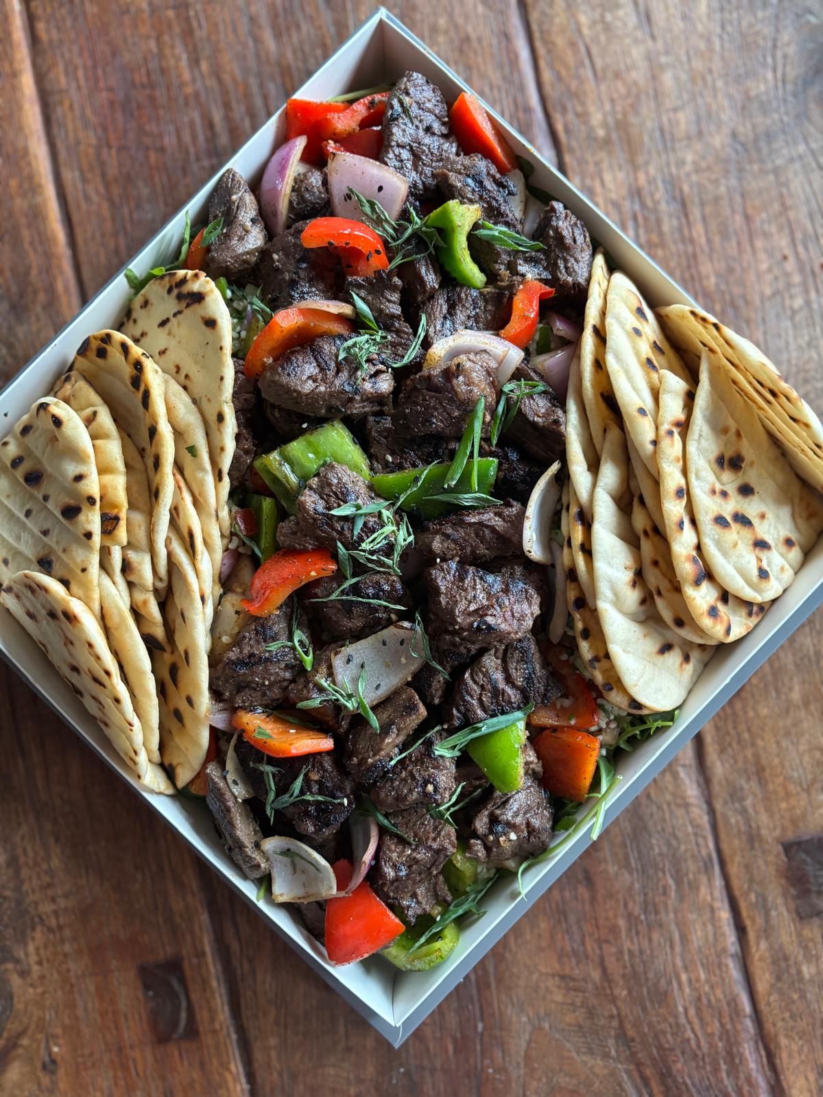 Plated dish of grilled meat with vegetables and naan bread on a wooden surface