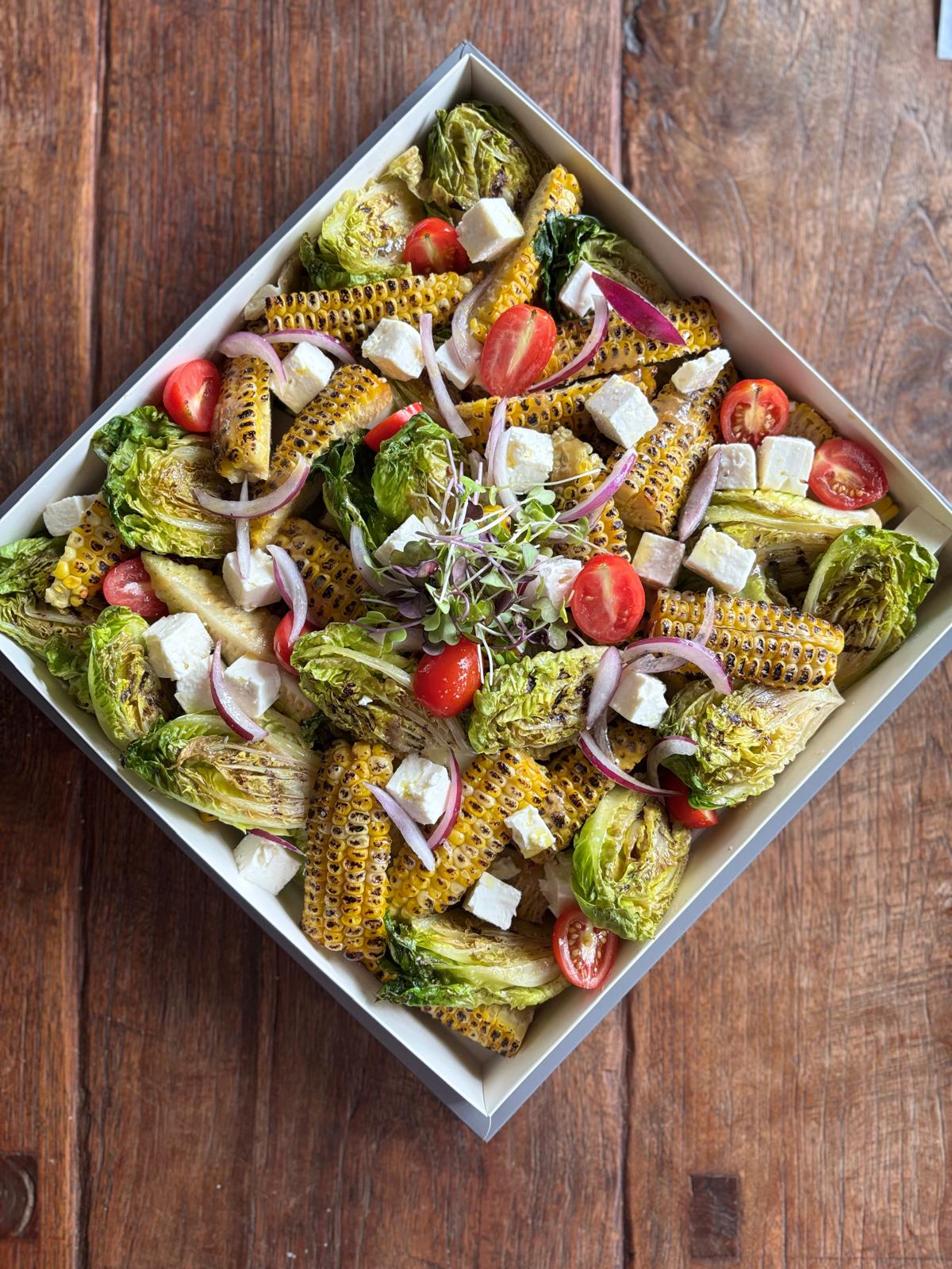 Salad with corn, tomatoes, and other vegetables in a white bowl on a wooden surface