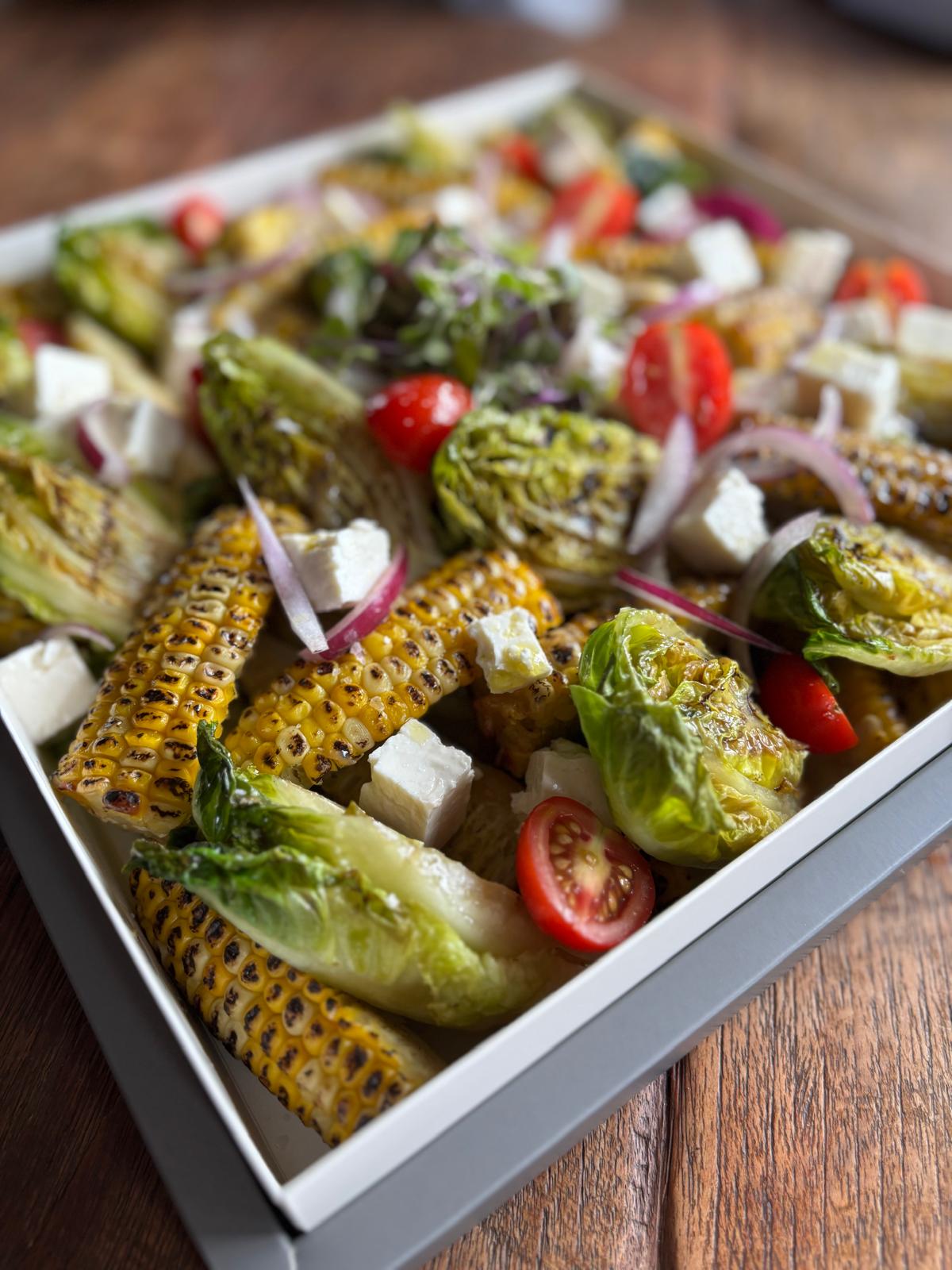 Salad with corn, tomatoes, and other vegetables in a white dish on a wooden table