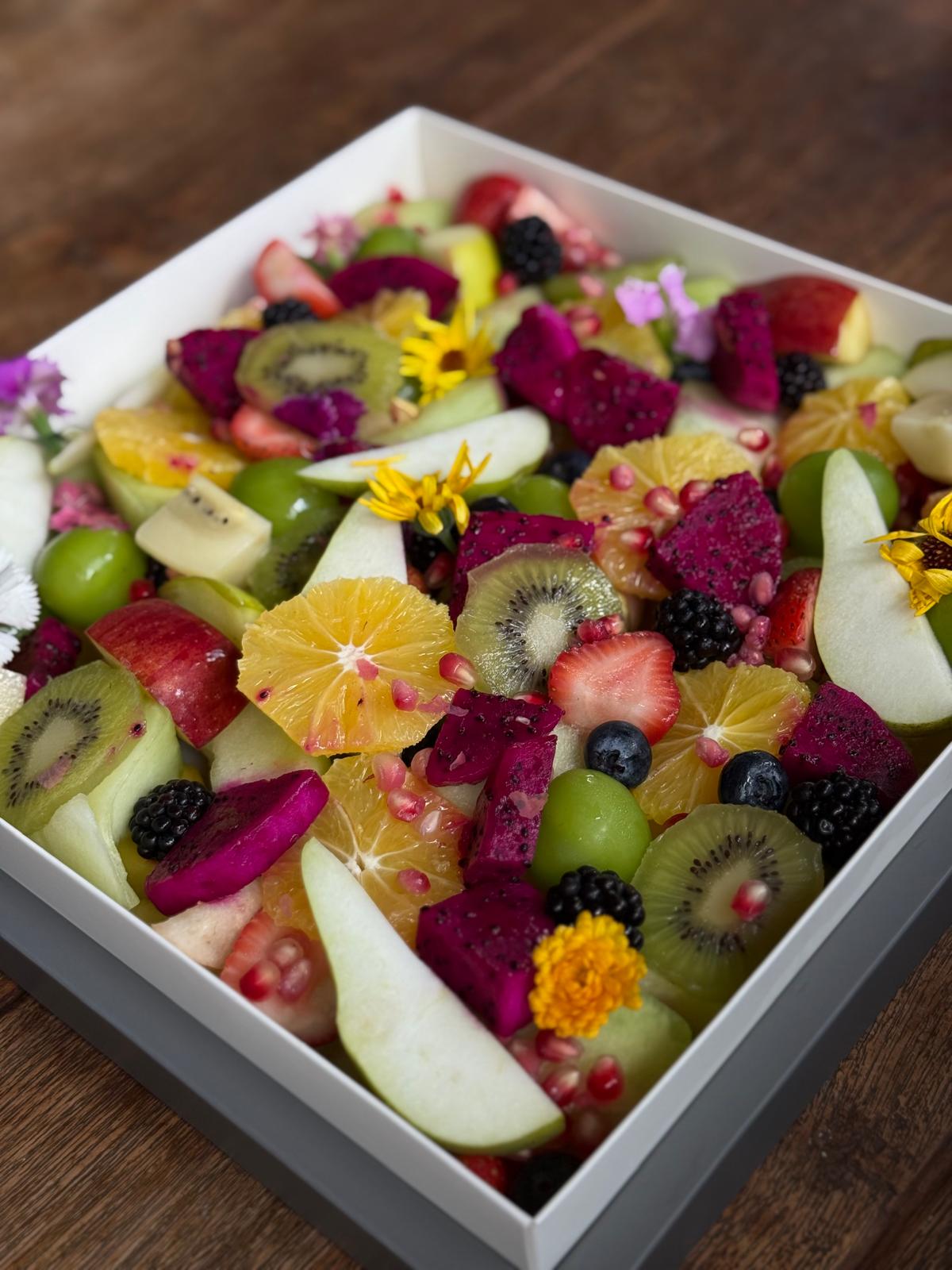 Colorful fruit salad with kiwis, strawberries, oranges, and other fruits in a white bowl on a wooden surface.