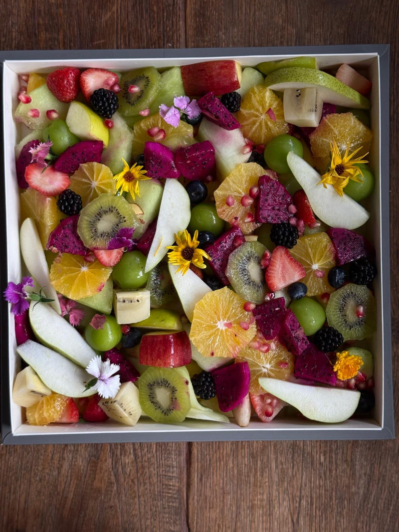 Assorted fruit salad with kiwis, strawberries, and oranges in a white bowl on a wooden surface.