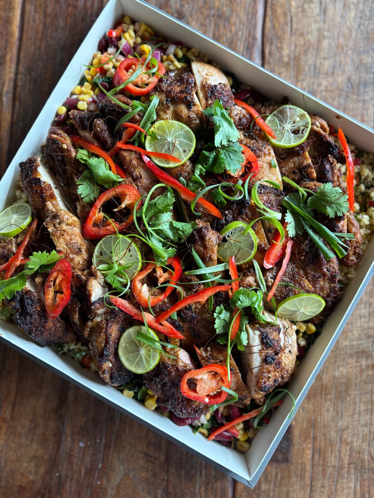 Plated dish of grilled chicken with vegetables and lime slices on a wooden surface