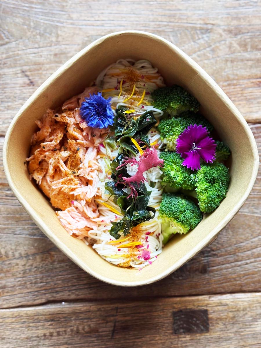 Salmon dish with vegetables and flowers on a wooden surface