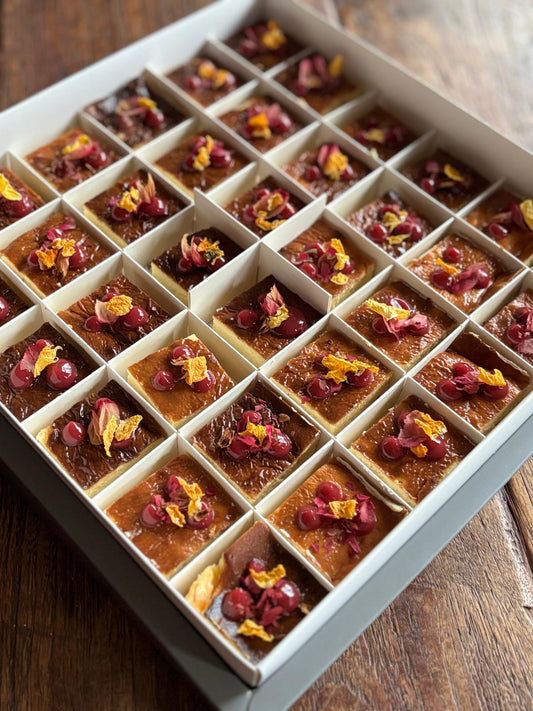 Small square pastries with dried flowers in a white box on a wooden surface