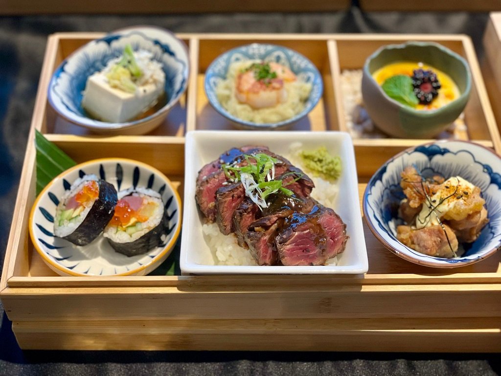 Assorted Japanese dishes on a wooden tray with a focus on a dish with sliced beef.