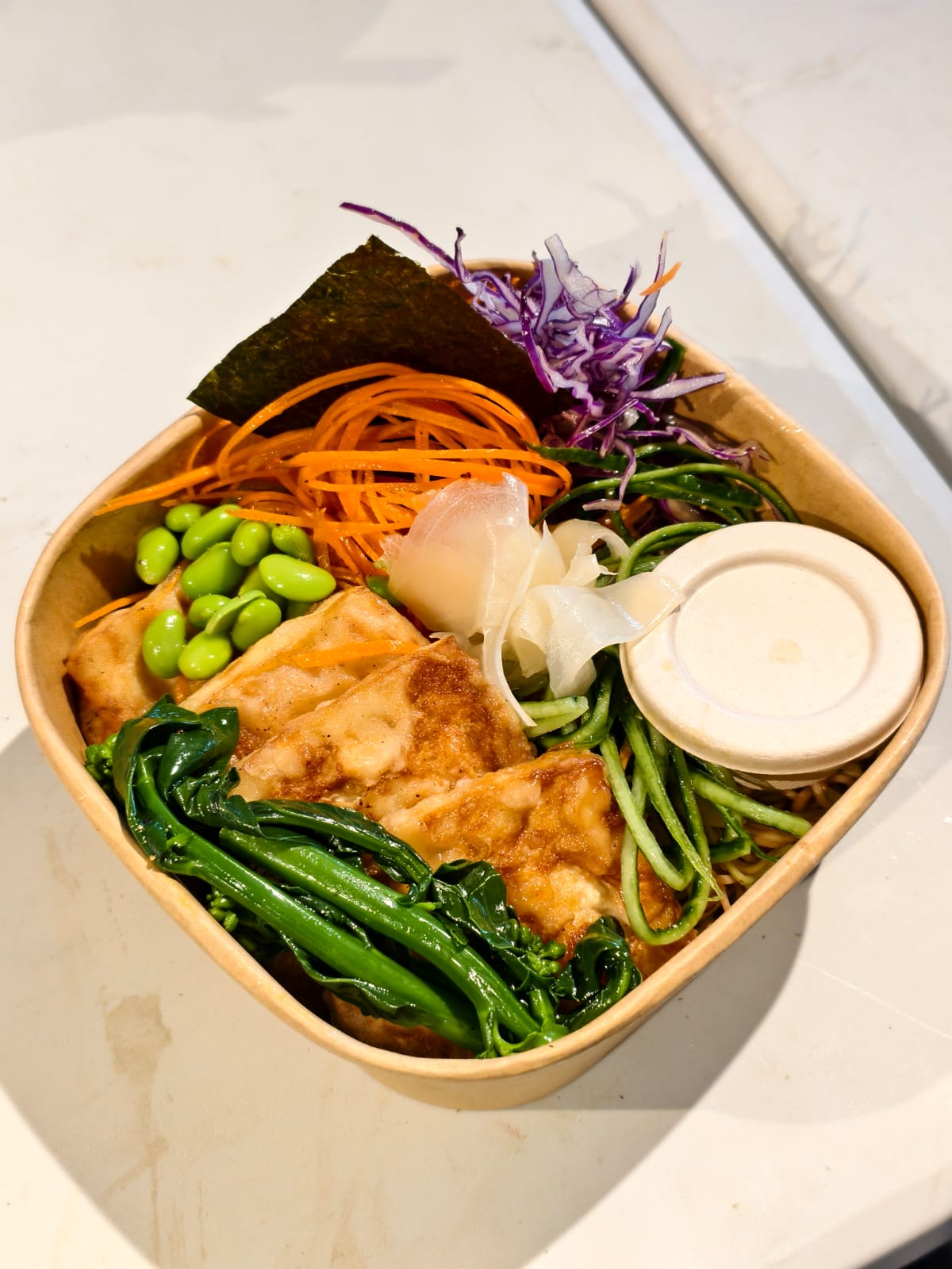 Bento box with assorted vegetables and tofu on a white surface