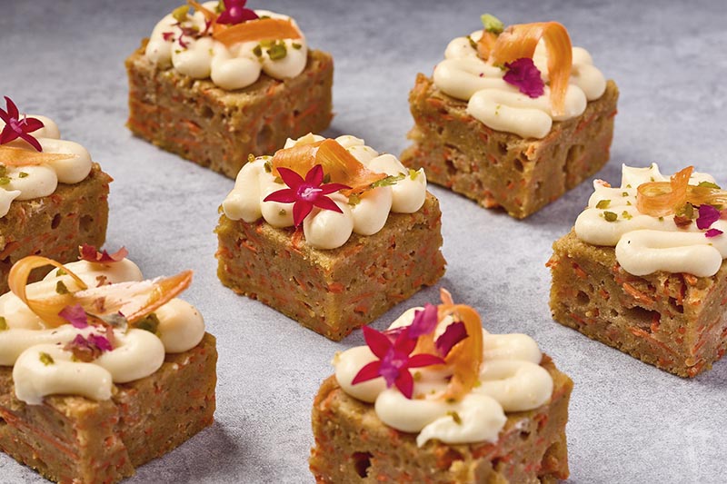 Carrot cake bars with cream cheese frosting and decorative flowers on a gray surface