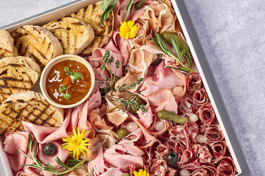 Platter of assorted meats and bread with a small bowl of sauce on a gray surface.