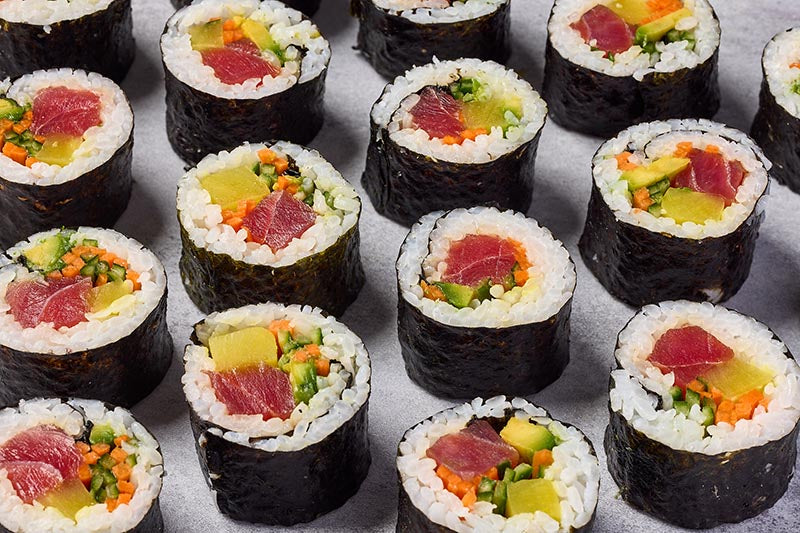 Assorted sushi rolls with various fillings on a light gray background