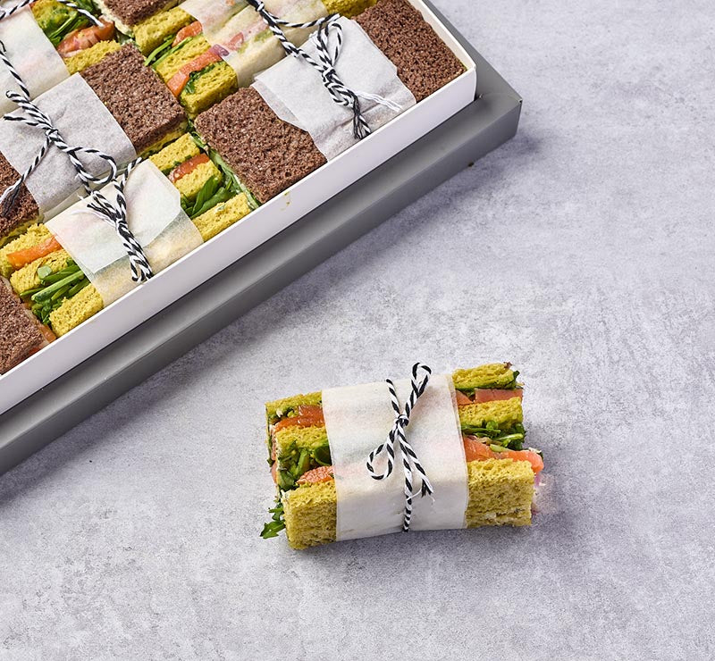 Bundled sandwiches on a gray surface with a tray in the background.