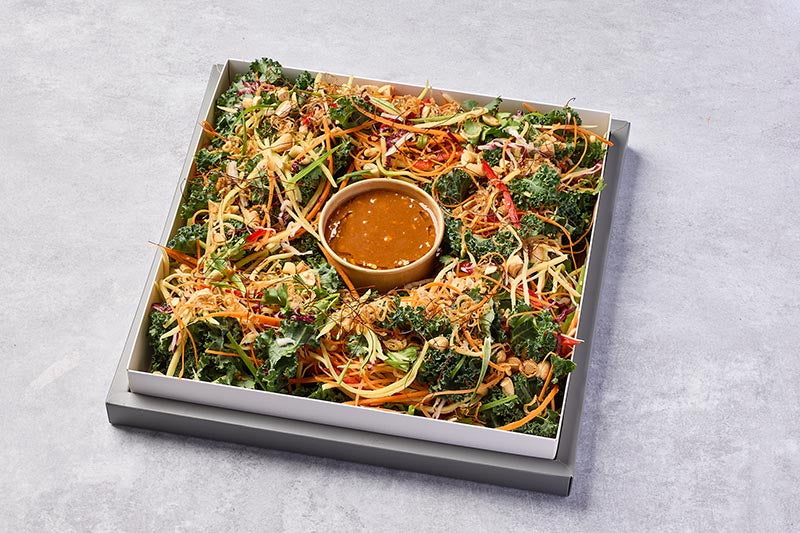 Colorful salad with a bowl of dressing on a gray surface