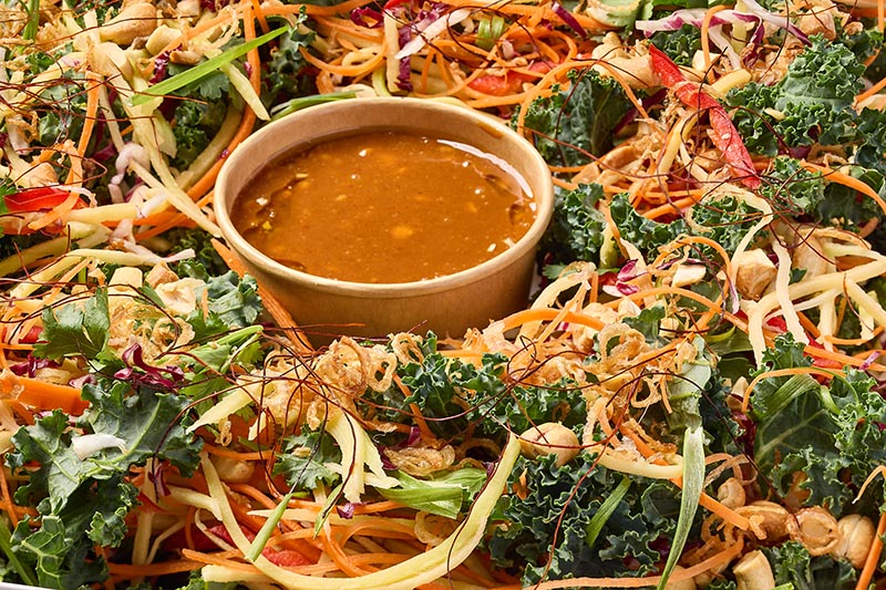 Colorful salad with kale, carrots, and other vegetables, topped with a small bowl of dressing.