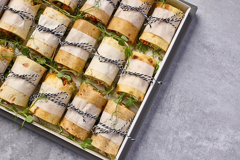 Rolled-up wraps wrapped in paper with string, placed on a gray surface.