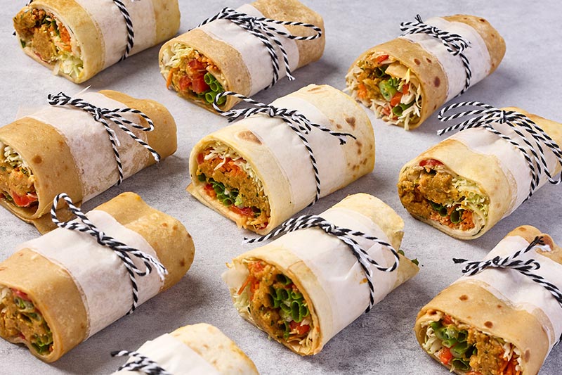Multiple sandwiches wrapped in tortillas with string on a gray surface