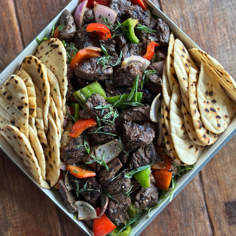 Plated dish of grilled meat with vegetables and naan bread on a wooden surface