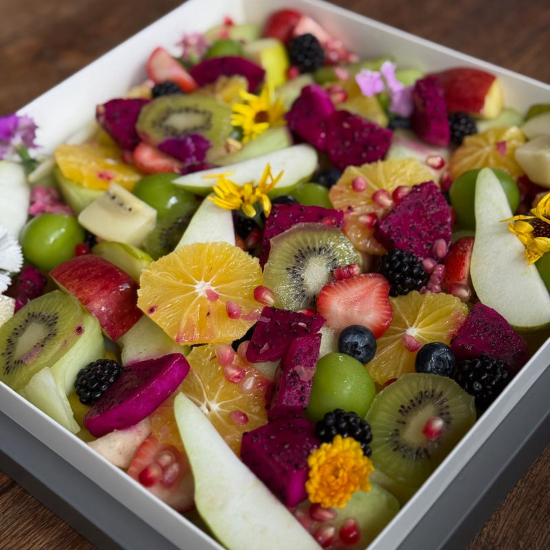Colorful fruit salad with kiwis, strawberries, oranges, and other fruits in a white bowl on a wooden surface.