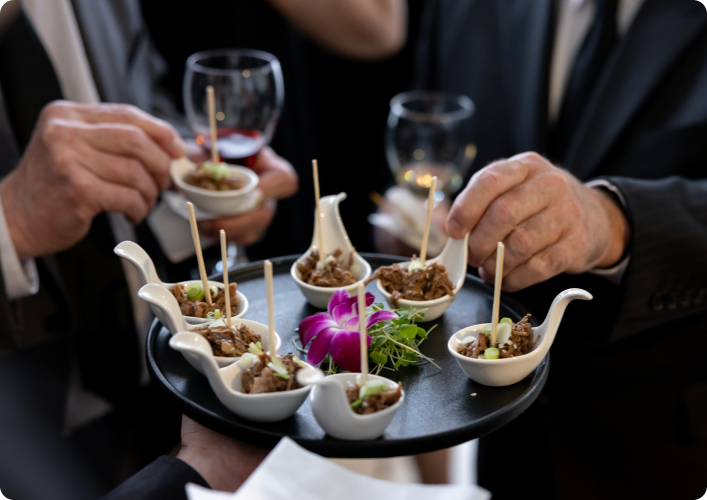Dessert canapés on a black tray with people in formal attire around