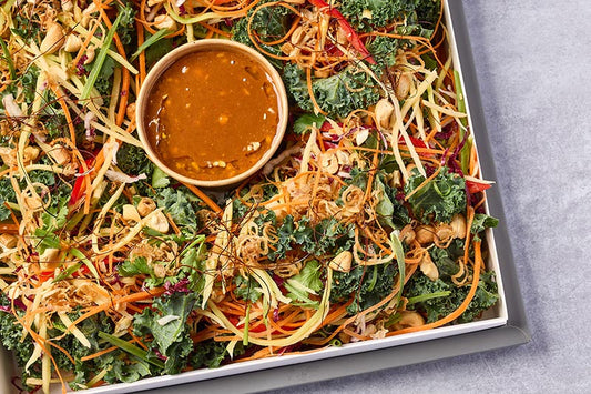 Vegetable salad with kale, carrots, and a small bowl of dressing on a gray surface.